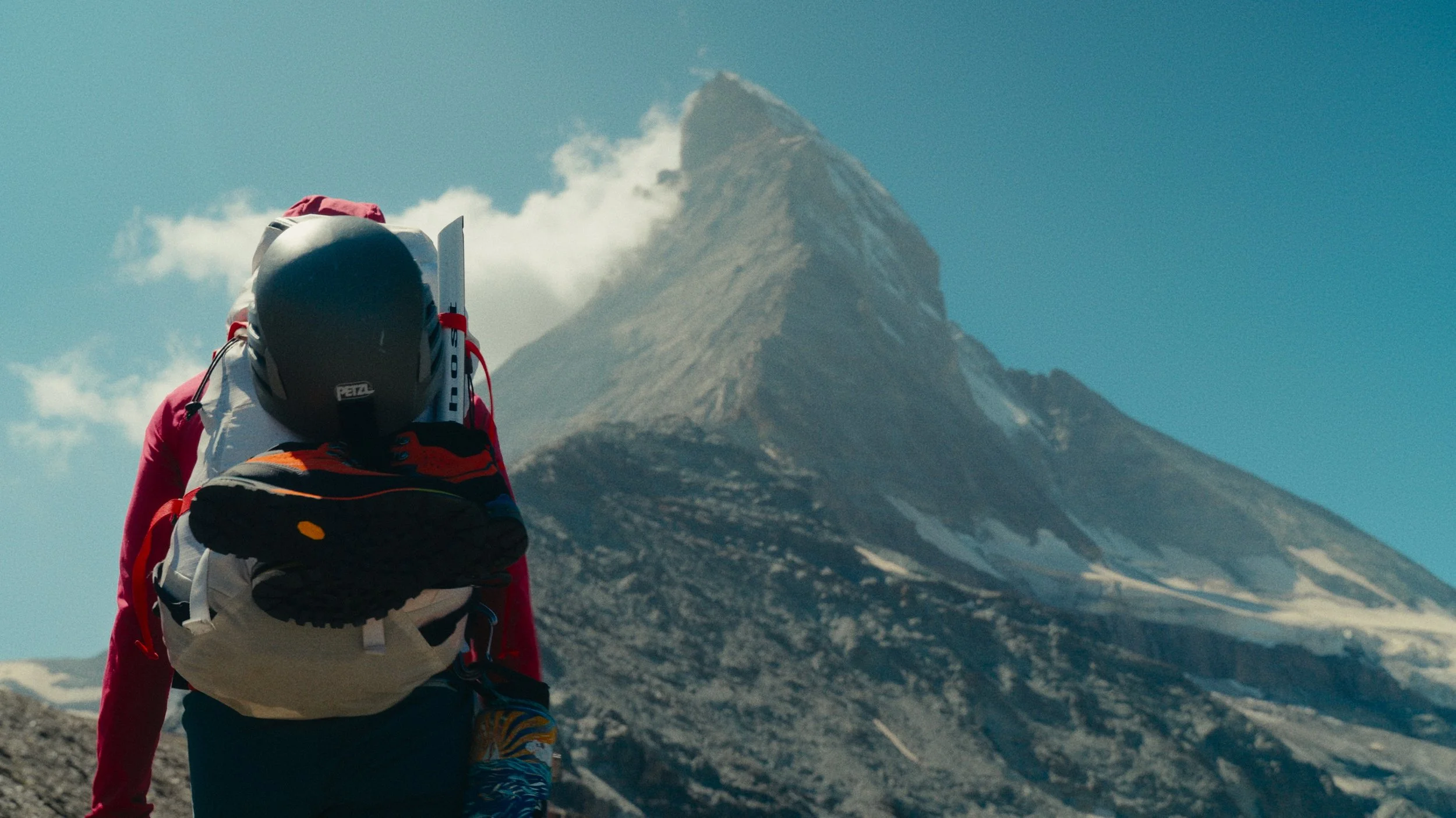 Mountain climber in gear ascending a rocky terrain with a snow-capped Swiss Matterhorn in the background as part of a behind the scenes photography shoot for a commercial outdoor video campaign.