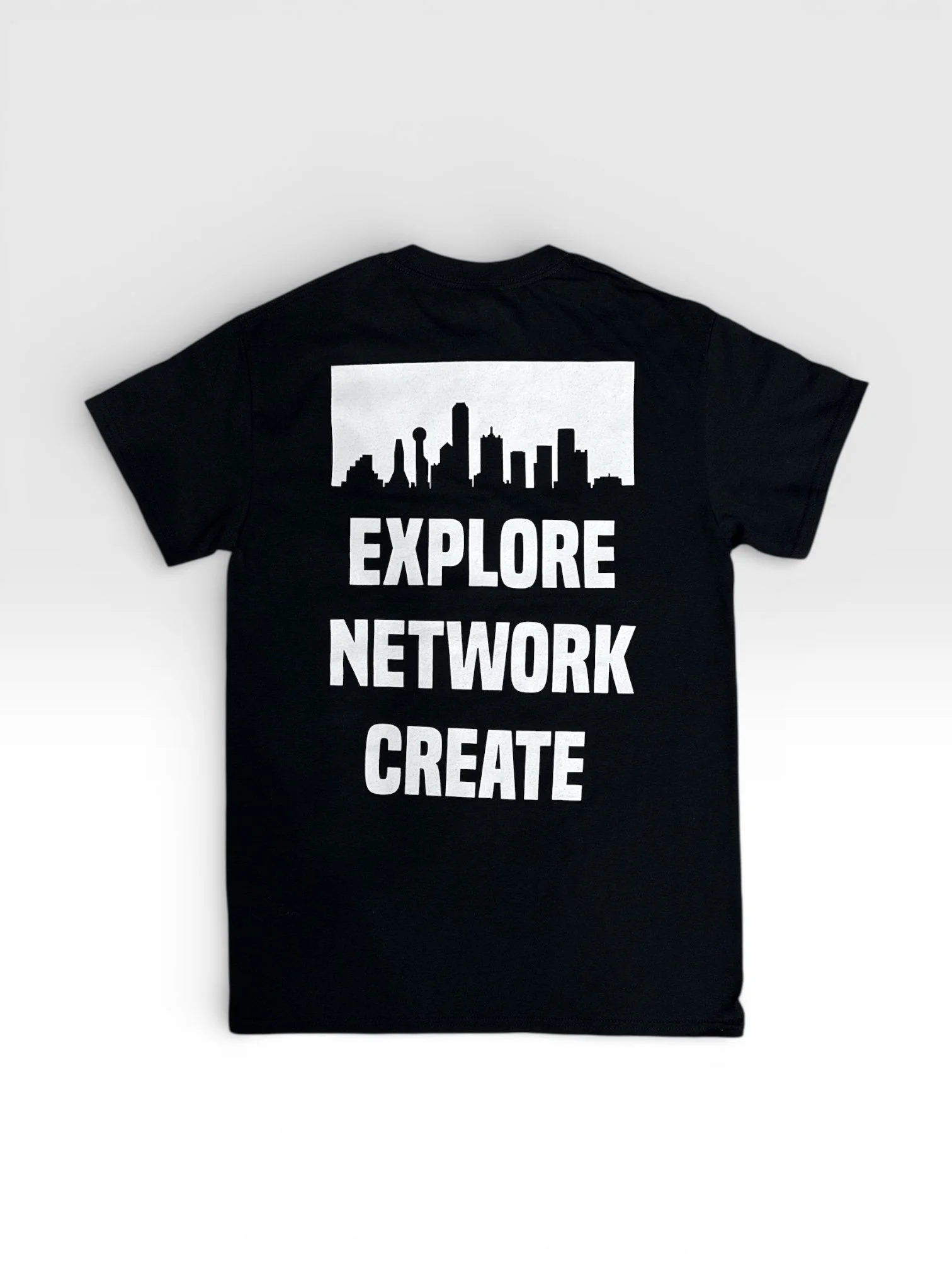 Back view of black DTXSTREET ORIGINALS Skyline Tee with white Dallas skyline graphic and bold text reading ‘Explore Network Create,’ modern urban streetwear apparel design