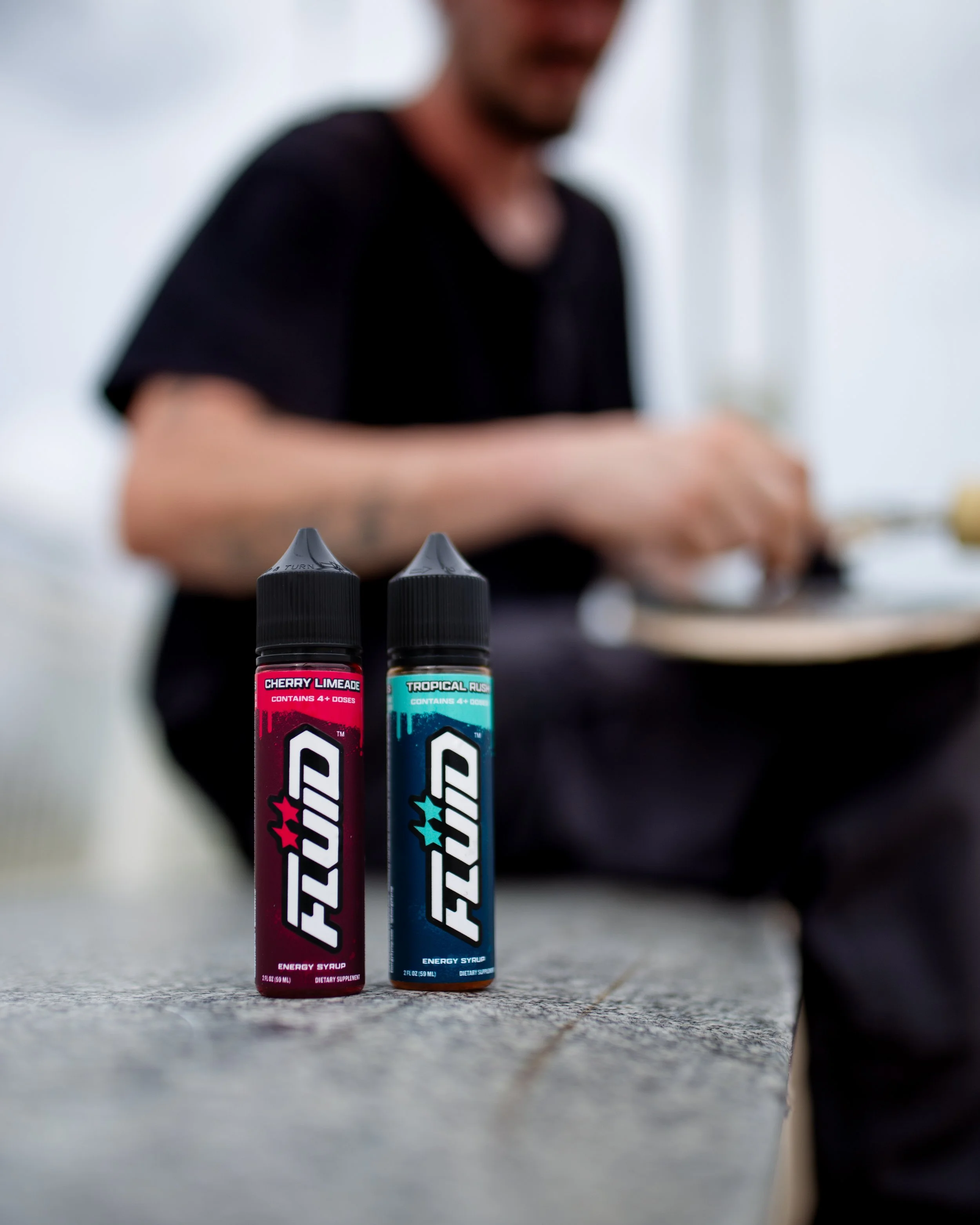 Two FLUID Energy Syrup bottles on a concrete ledge with a person working on a skateboard in the background