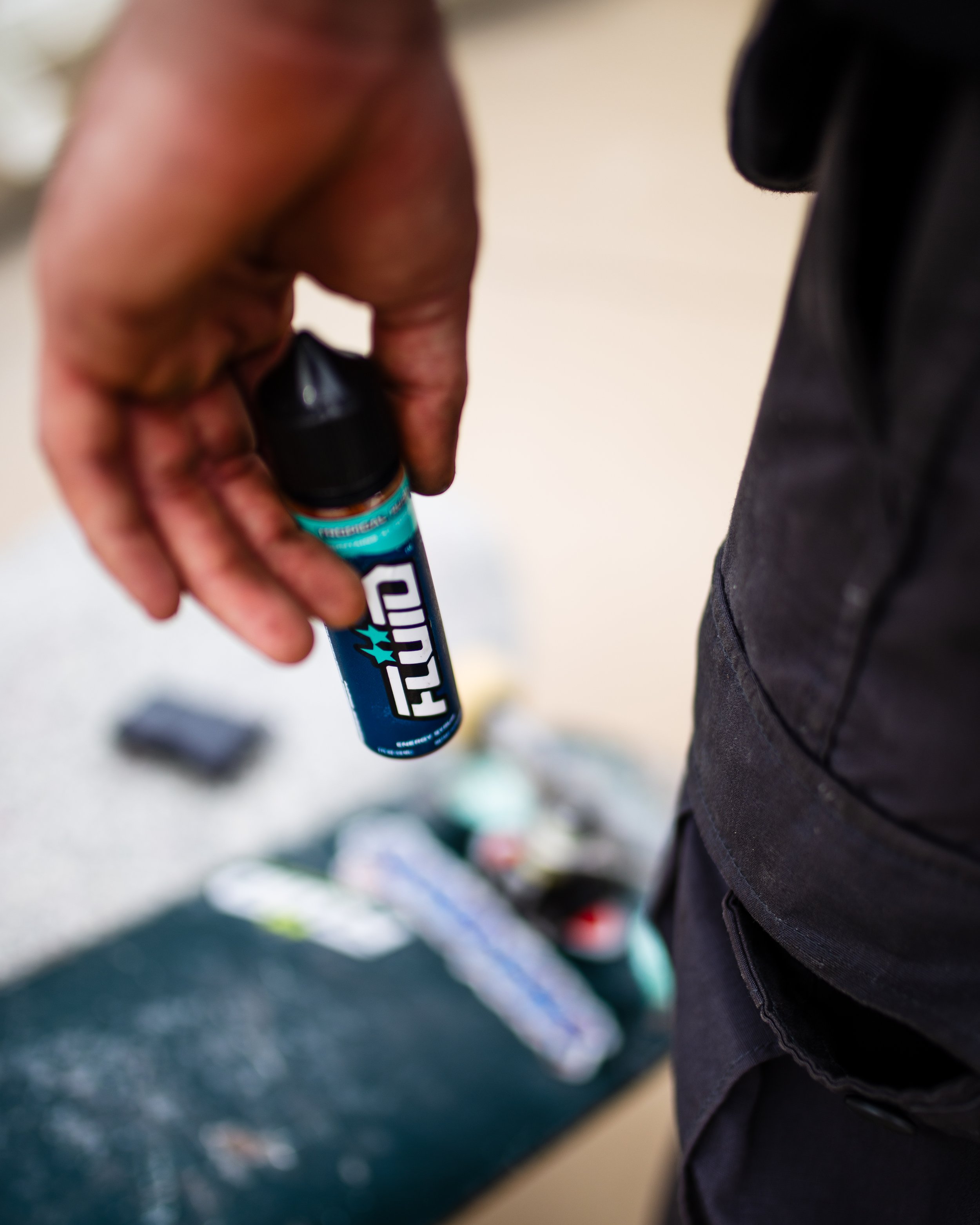 Hand holding a blue-labeled FLUID Energy Syrup bottle beside a skateboard in an outdoor setting