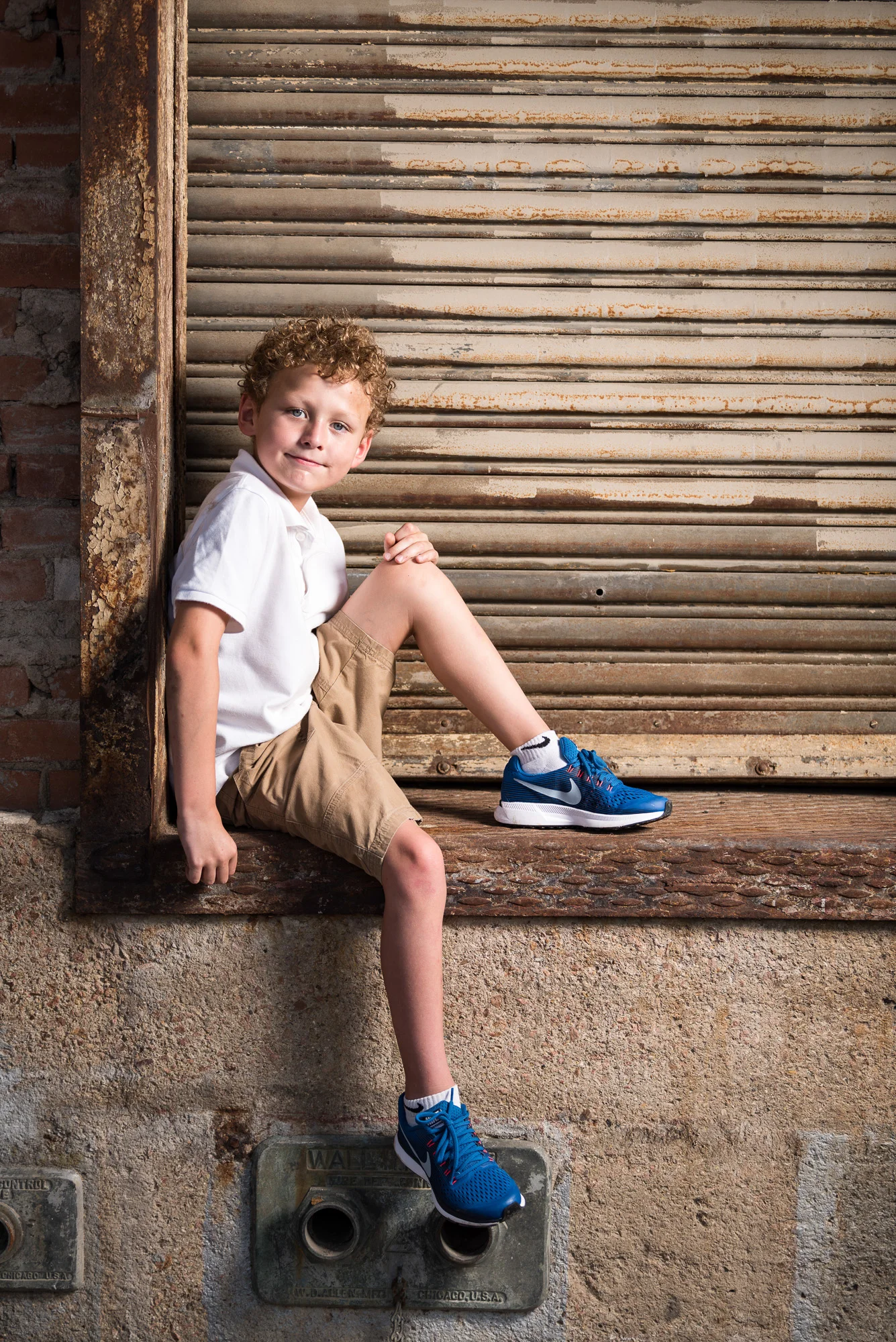 boy child children blue eyes side seating white tshirt school uniforms rusty door loadking duck downtown fort worth old post office warm light studio flash on location side curly dark hair smile smiling love 9 years_.jpg