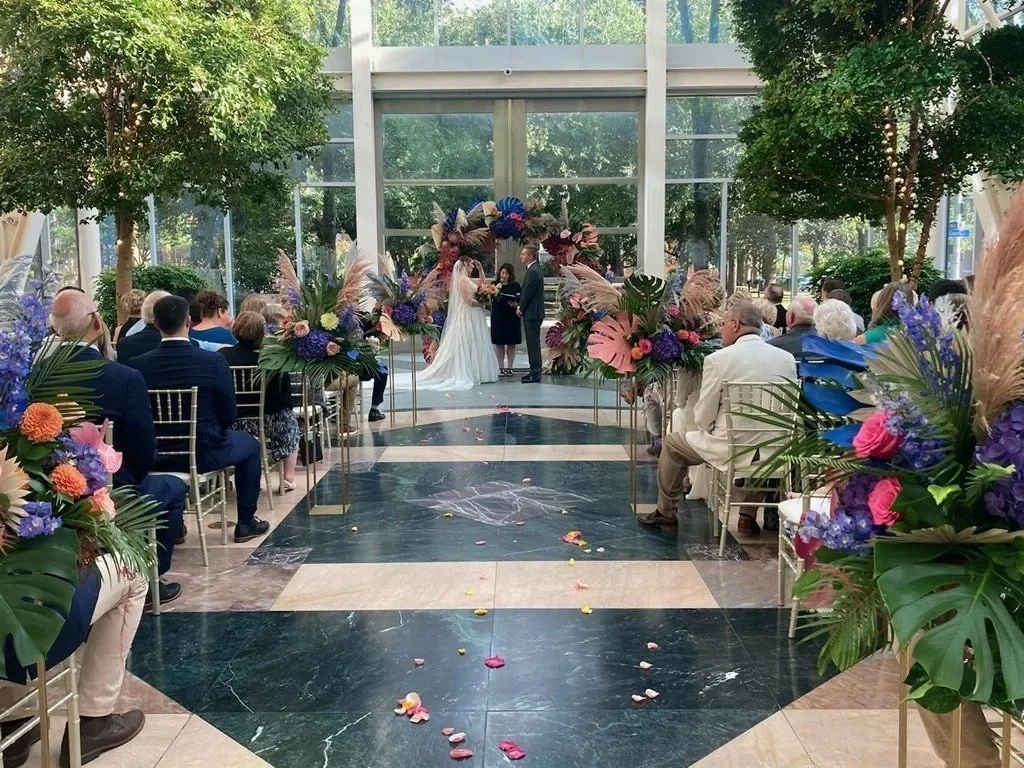 a man and woman at a wedding with an officiant in front of a very colorful circle arch
