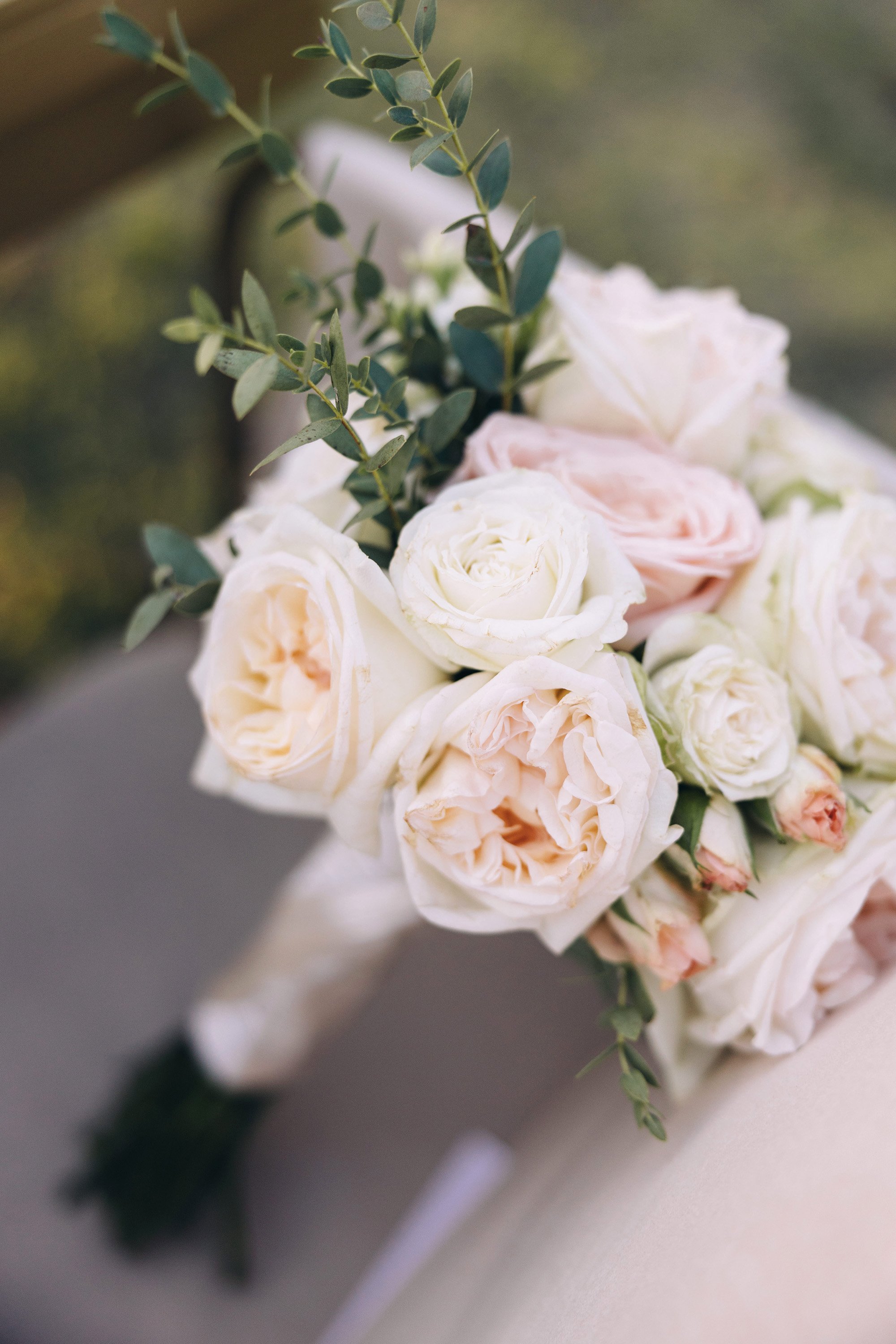 A bouquet of white and blush pink roses with green foliage on a blurred background.