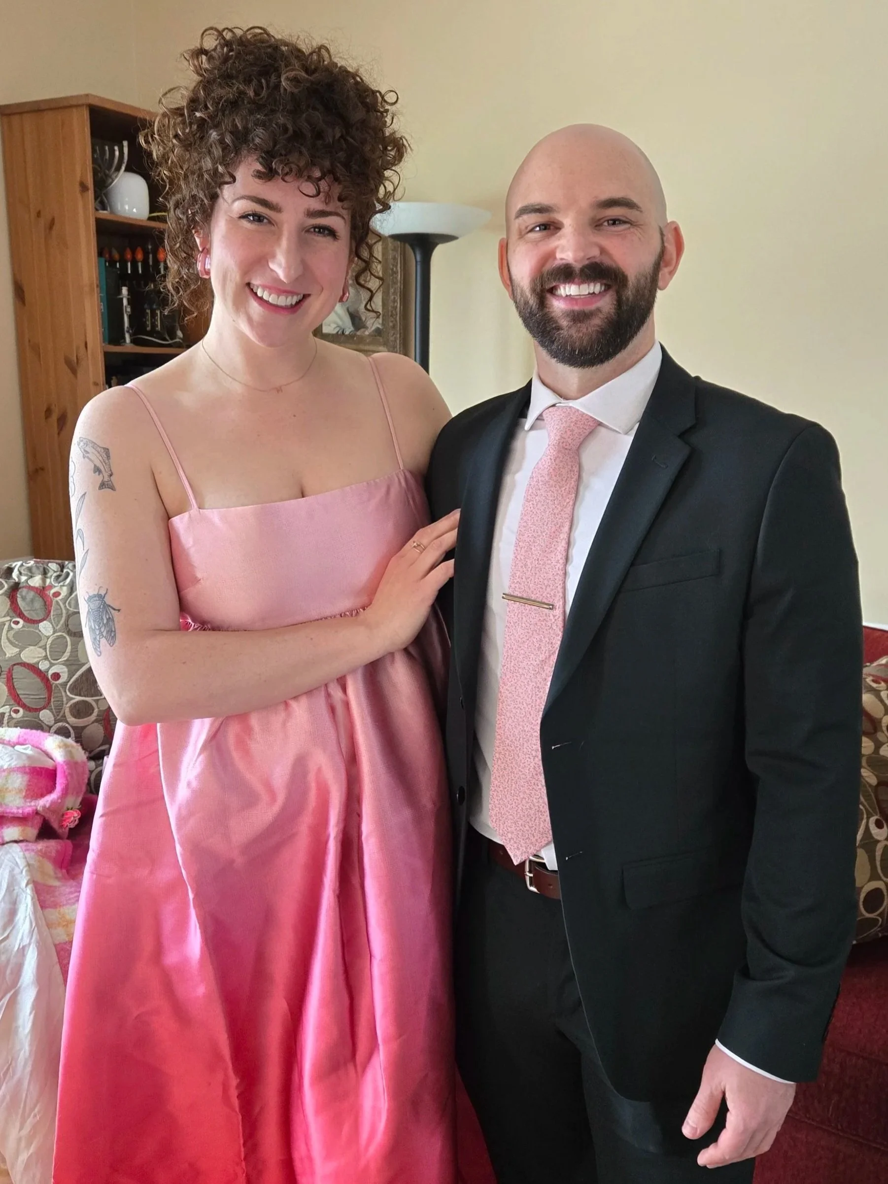Woman in an ombre pink dress holding the arm of a man in a black suit and pink tie smiling
