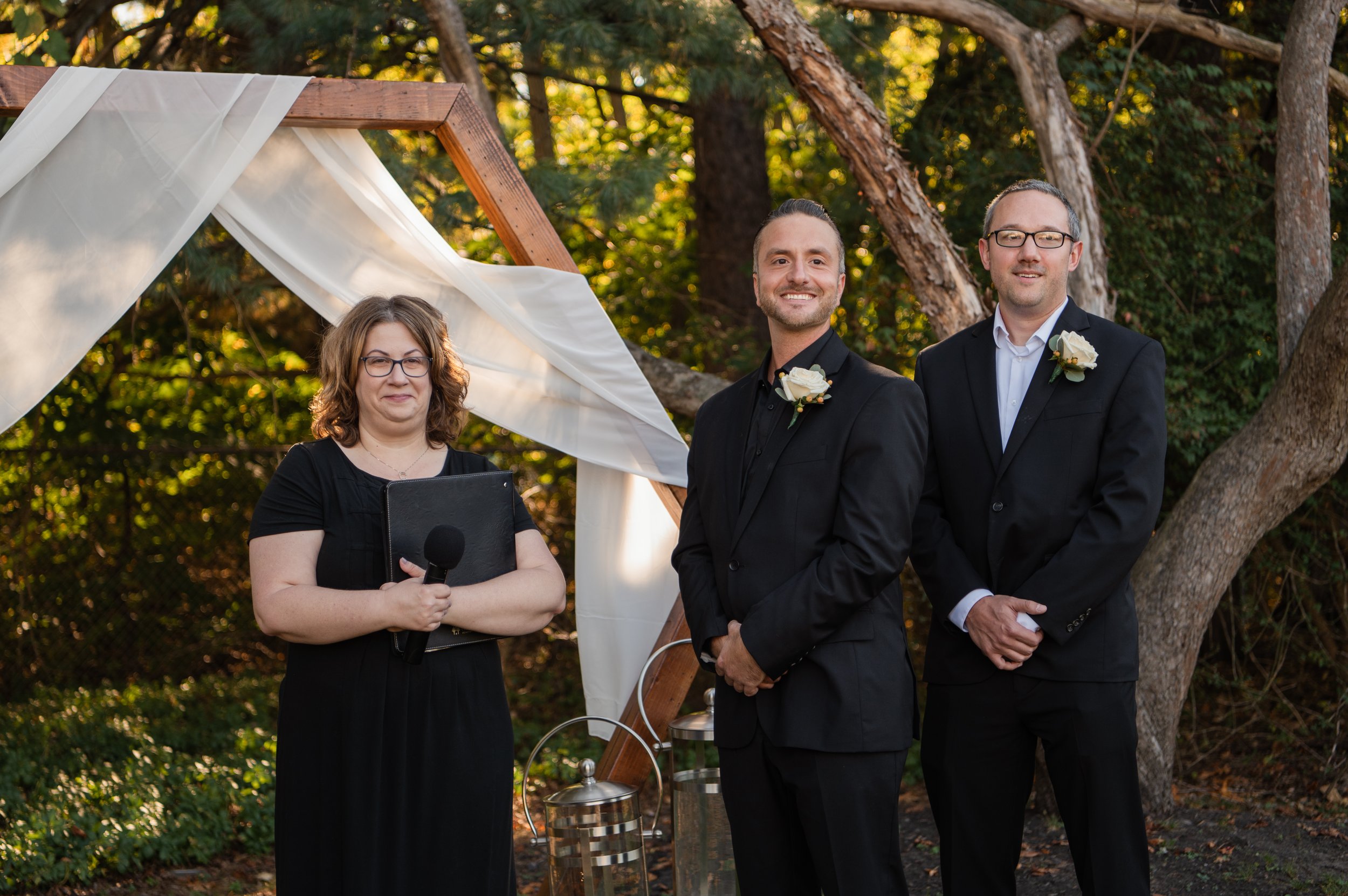 Groom and Best Man dressed on black waiting at a hexagon arch with the officiant for the bride