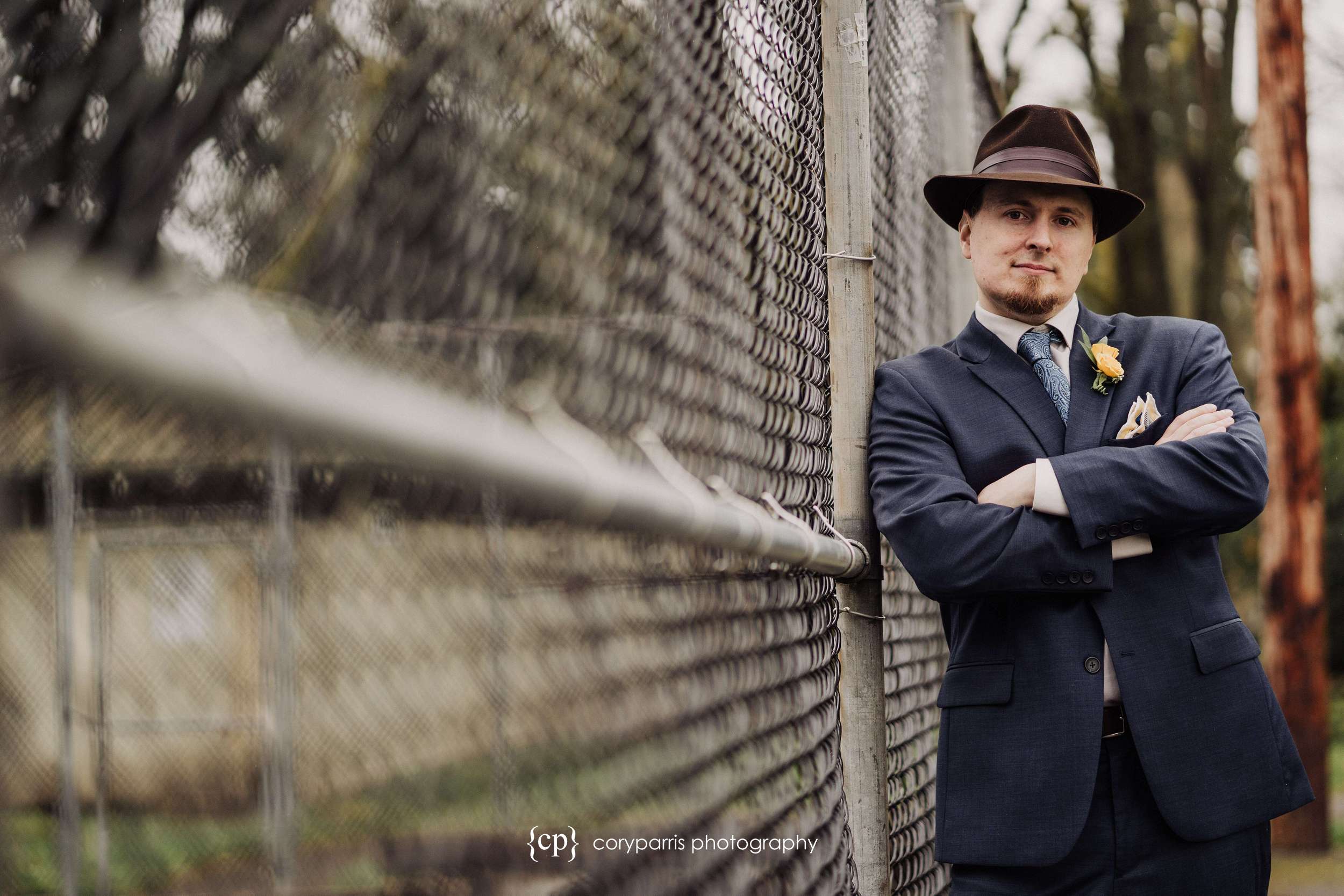 Groom in hat posing next to a fence before everett wedding