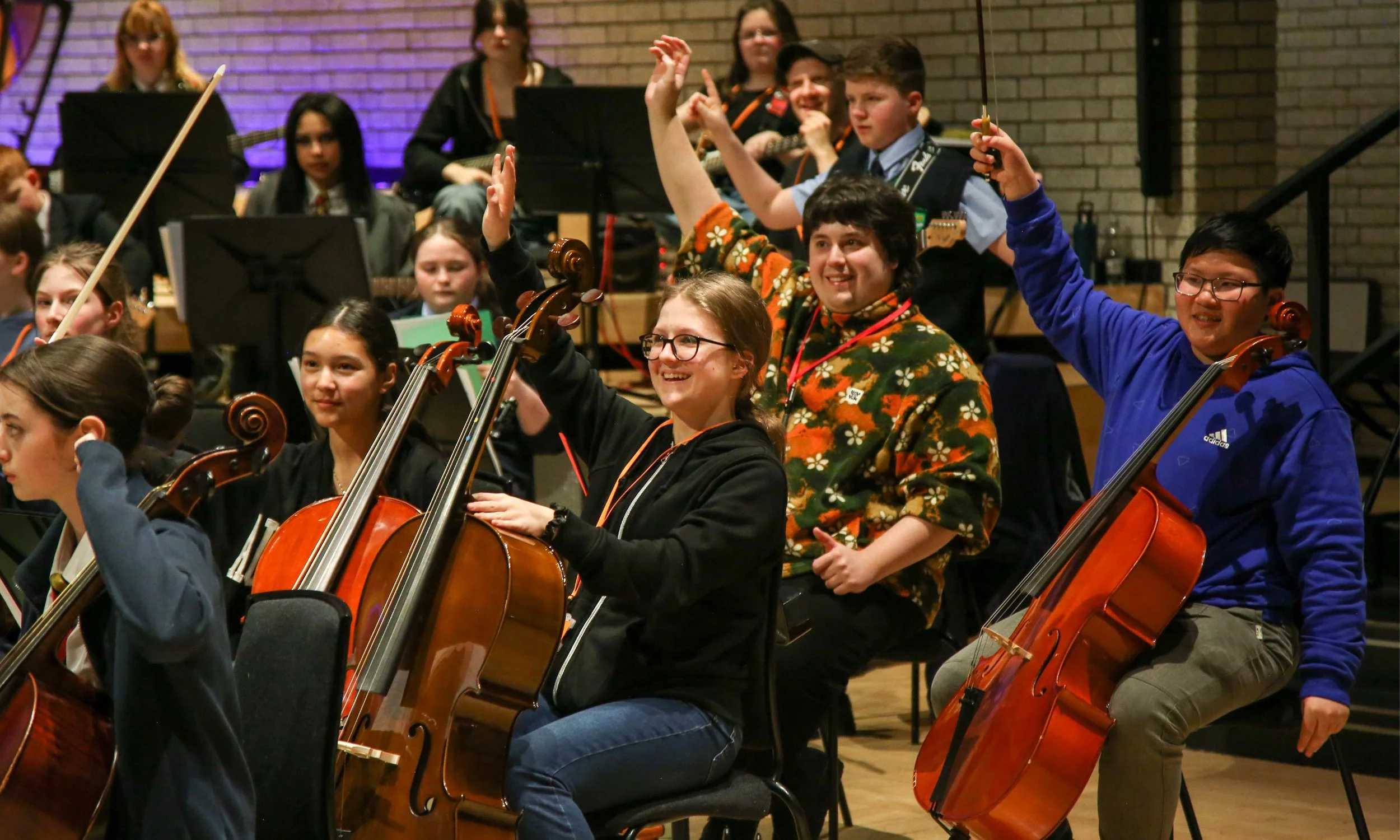 The cello section of a Modulo ensemble at the Royal Northern College of Music. The musicians have their hands in the air.