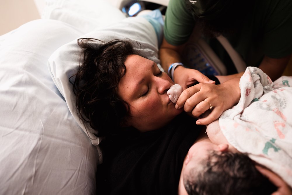 mother kisses baby hands just after hospital birth