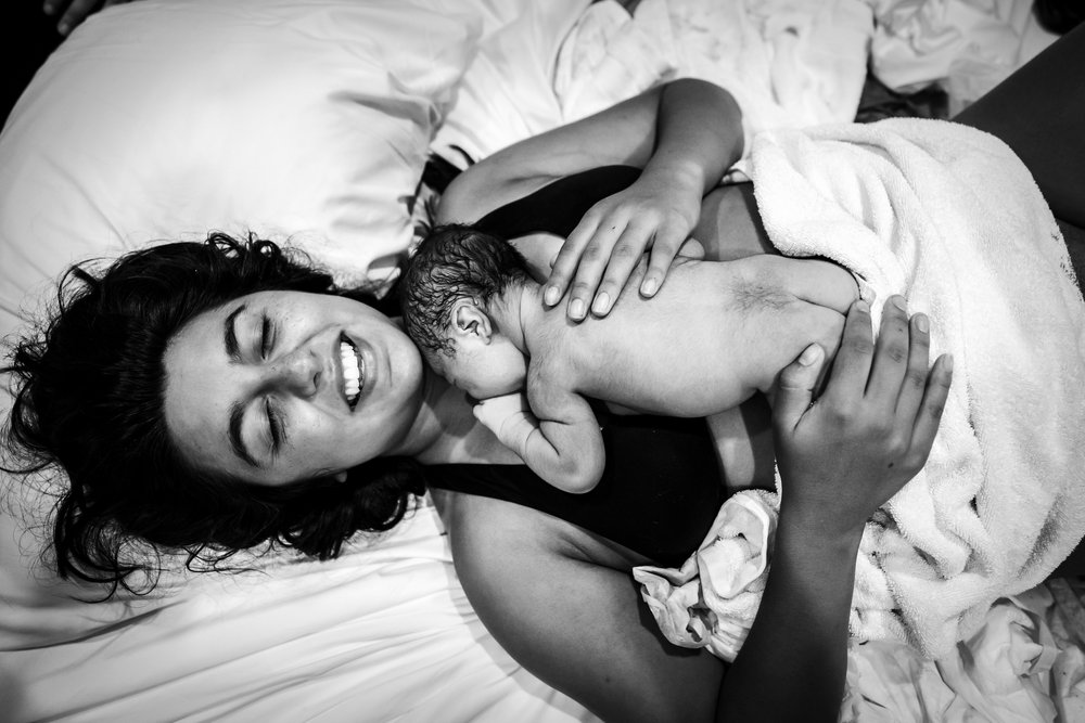 mother smiles holding newborn after home birth