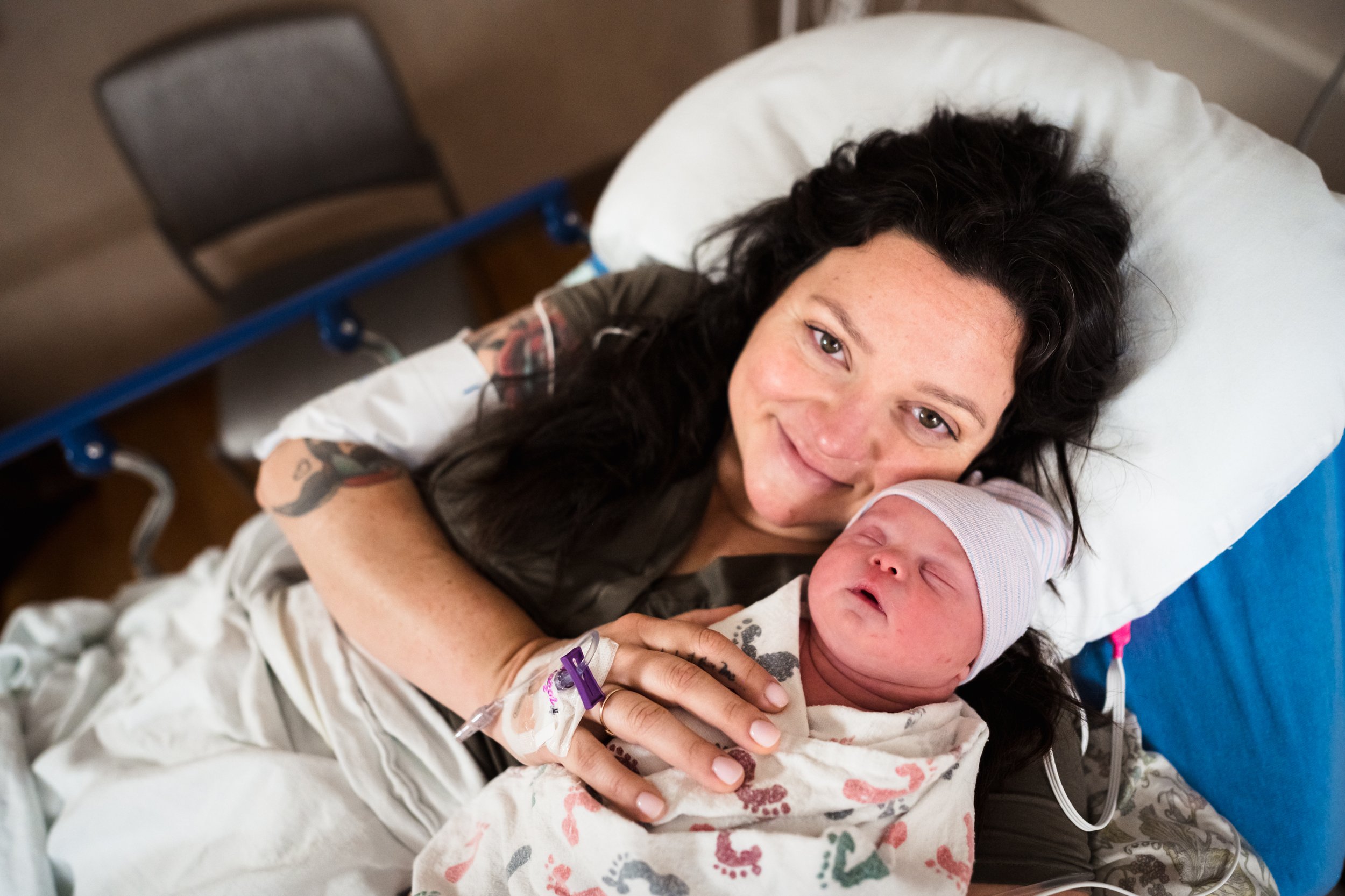 mother looks at camera while holding newborn baby wrapped in hospital swaddle after birth