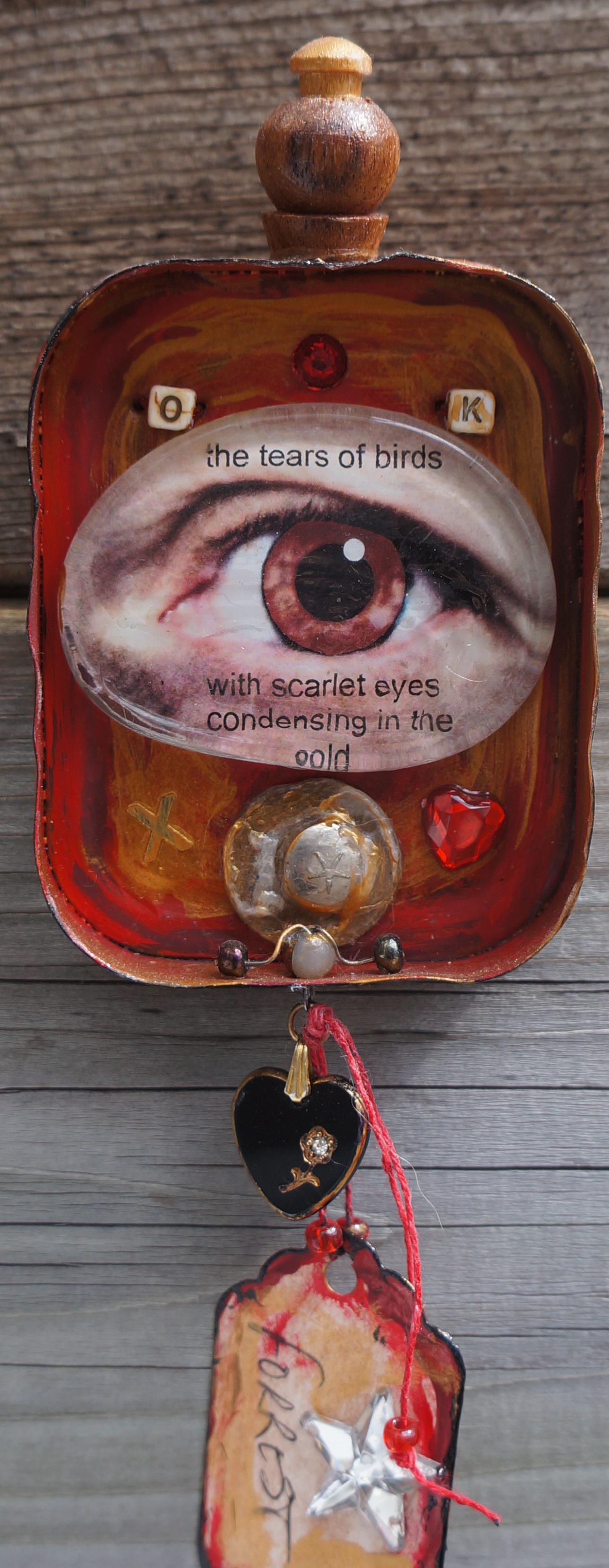 Mixed media collage in the lid of a corned beef tin. Found objects, glass glob with photograph of my eye, tag, beads, paint.