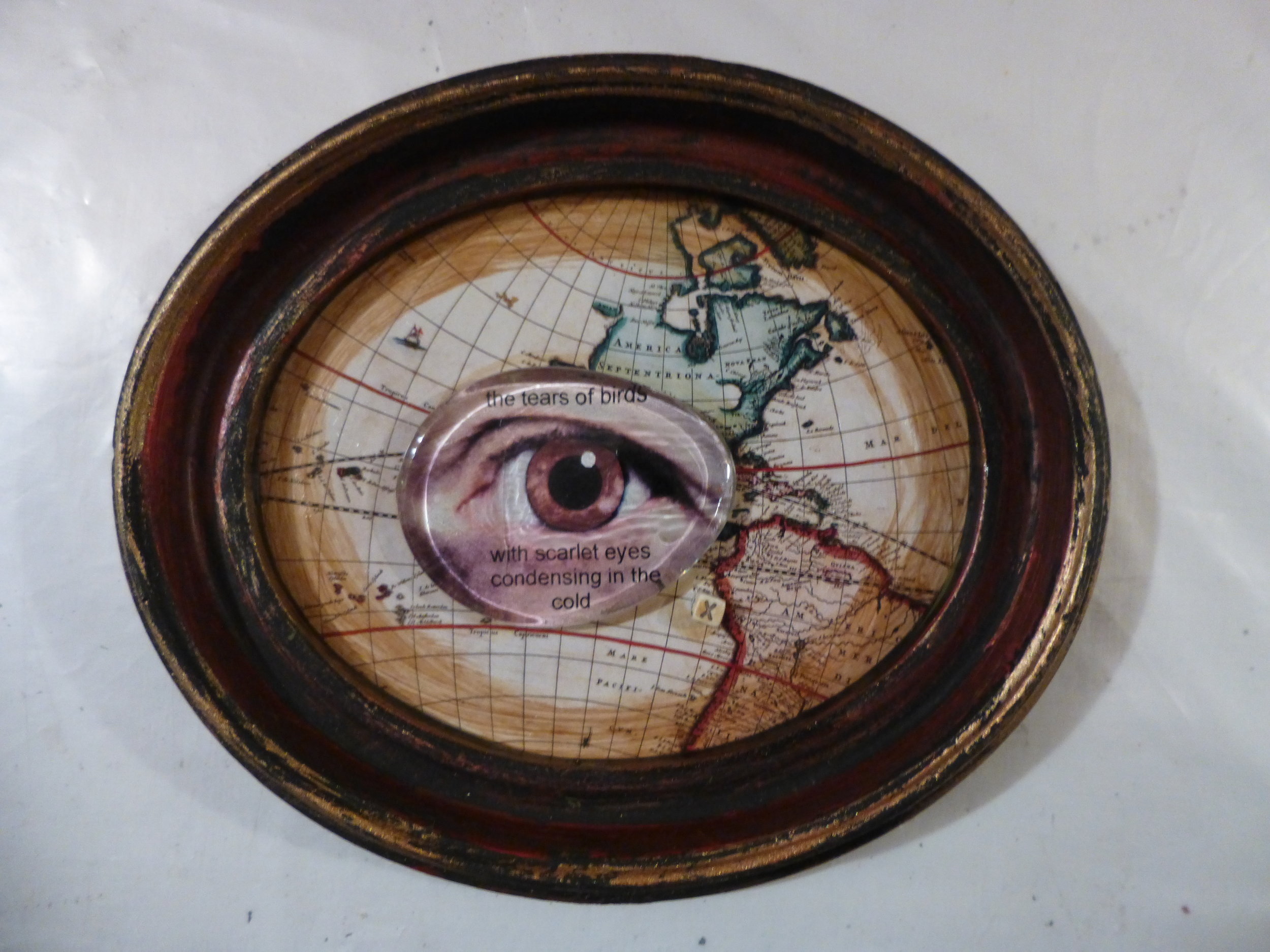 Mixed media collage. Small oval recycled frame from the thrift shop, glass glob, photograph of my eye, old map from a calendar, paint.