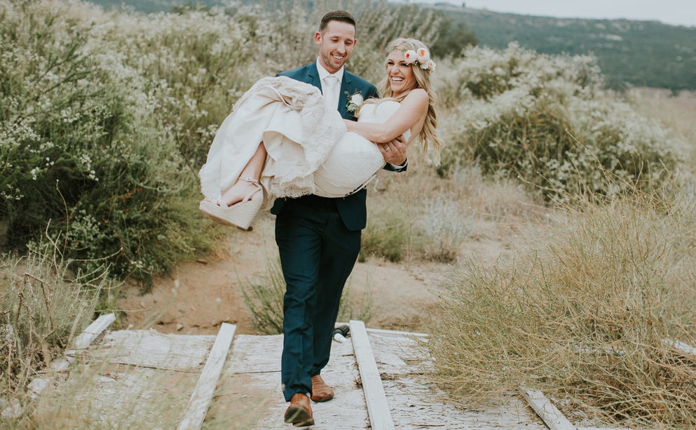 Wedding Photos Outdoors with Husband Carrying Bride. Bridal Hair and Makeup by Vanity Belle in Orange County (Costa Mesa) and San Diego (La Jolla)