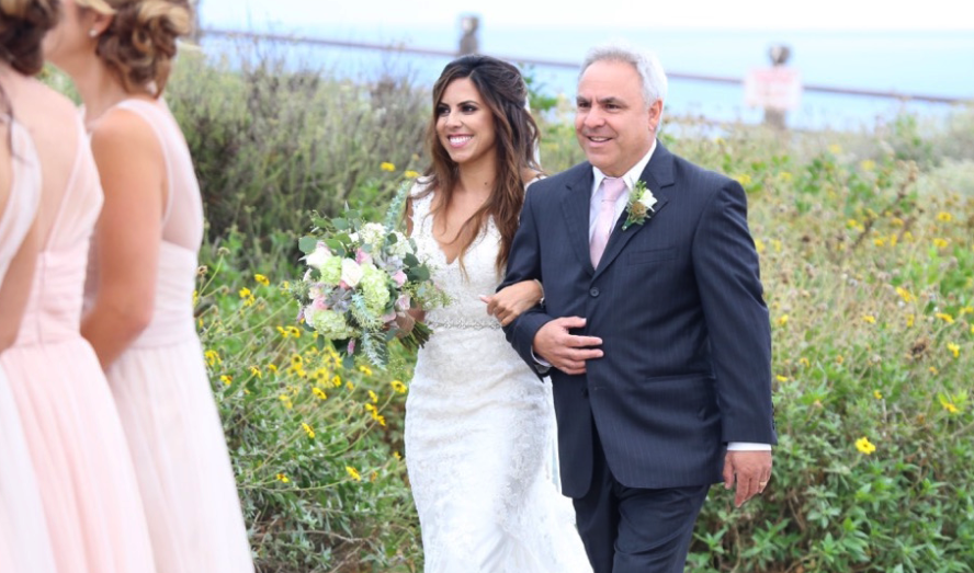 Brunette Bride Walking Down Aisle outside holding Bouquet in Wedding Photos. Bridal hair and makeup by Vanity Belle in Orange County (Costa Mesa) and San Diego (La Jolla)