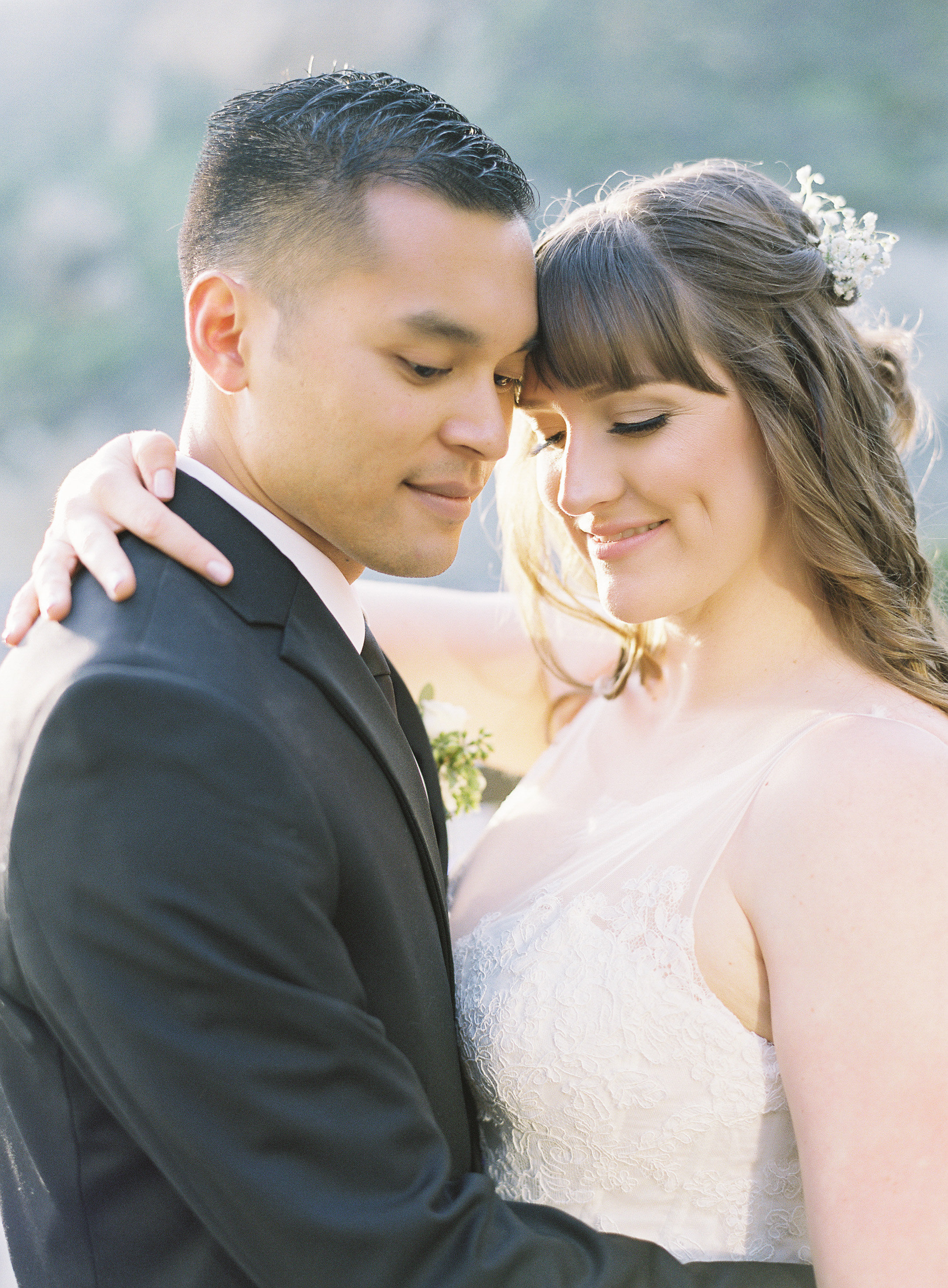 Brunette Bride with Bangs and Hair Down Hugging Husband outdoors. Wedding Hair and Makeup by Vanity Belle in Orange County (Costa Mesa) and San Diego (La Jolla)