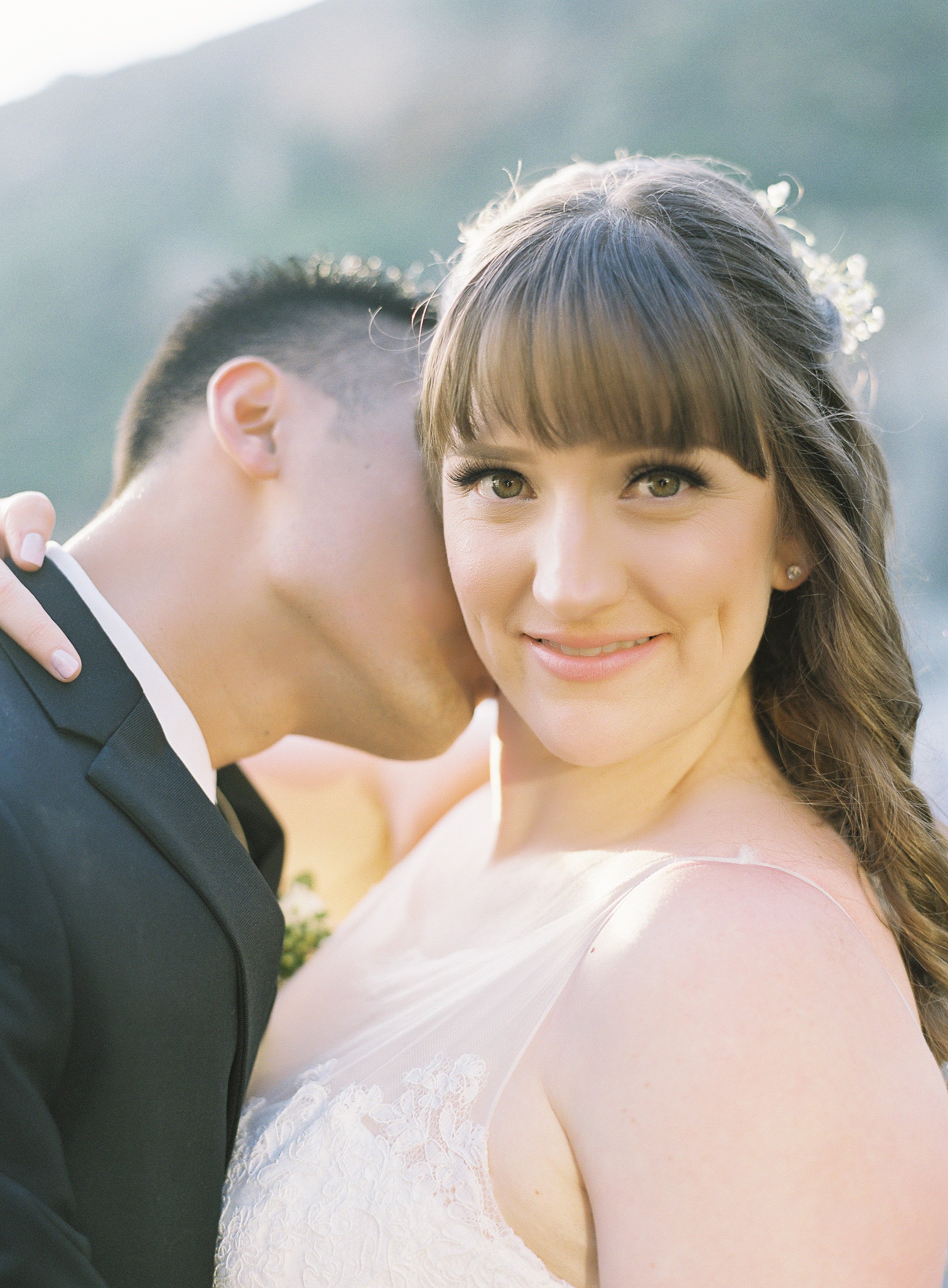 Brunette Bride with Bangs and Hair Down with Husband Kissing Neck. Wedding Hair and Makeup by Vanity Belle in Orange County (Costa Mesa) and San Diego (La Jolla)