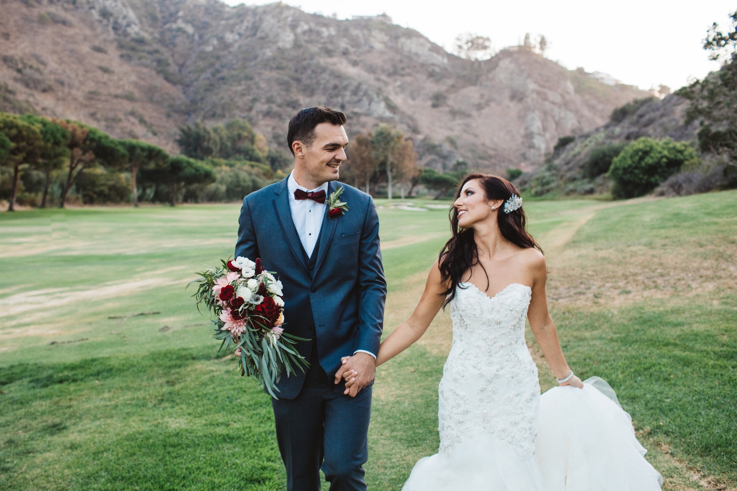 Brunette Bride with Long Hairstyle Down holding hands with Husband in Outdoor Wedding Photos. Bridal hair and makeup by Vanity Belle in Orange County (Costa Mesa) and San Diego (La Jolla)