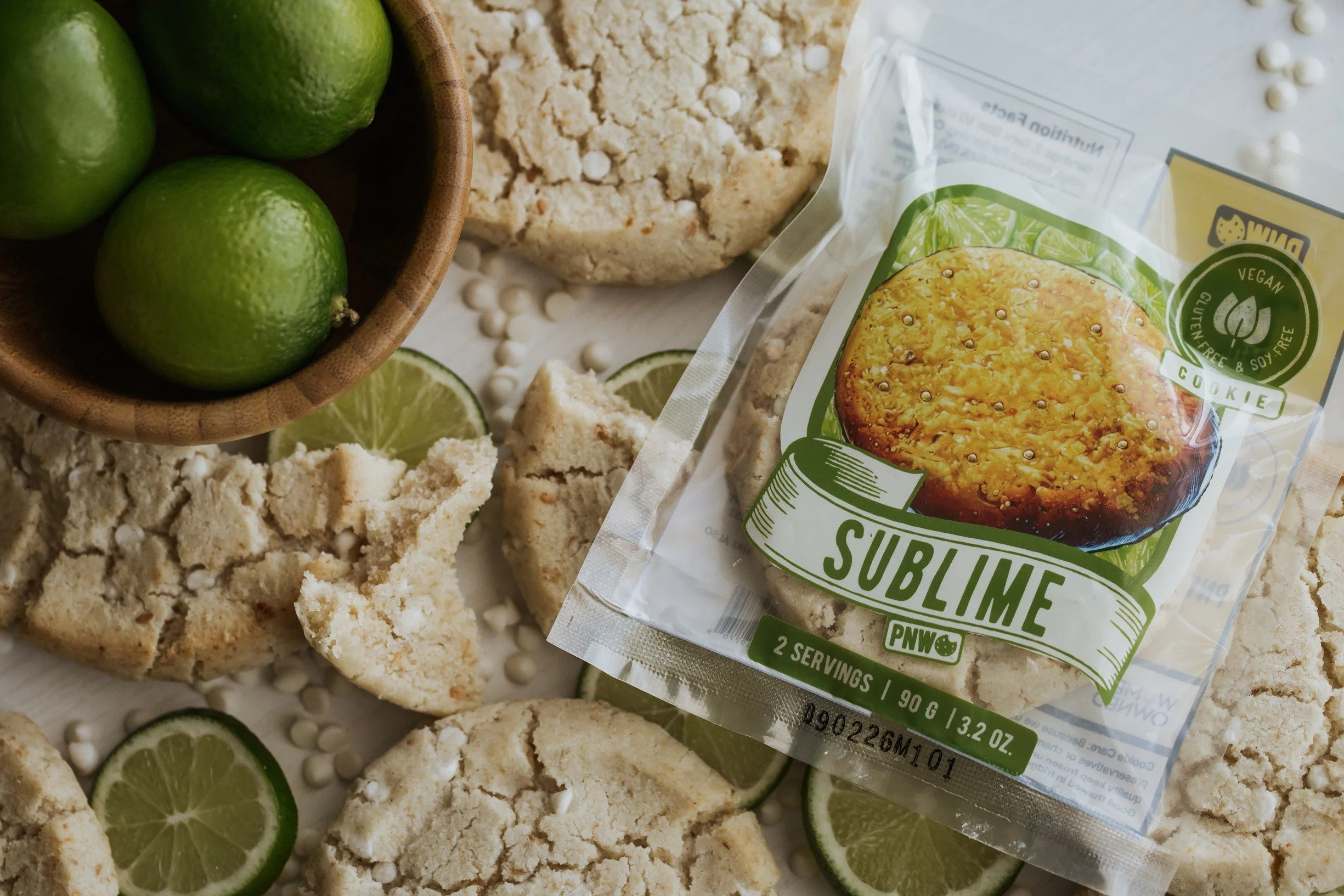 Lime slices, vegan gluten free cookie package, crumbled cookies, and lime in a bowl on a white surface.