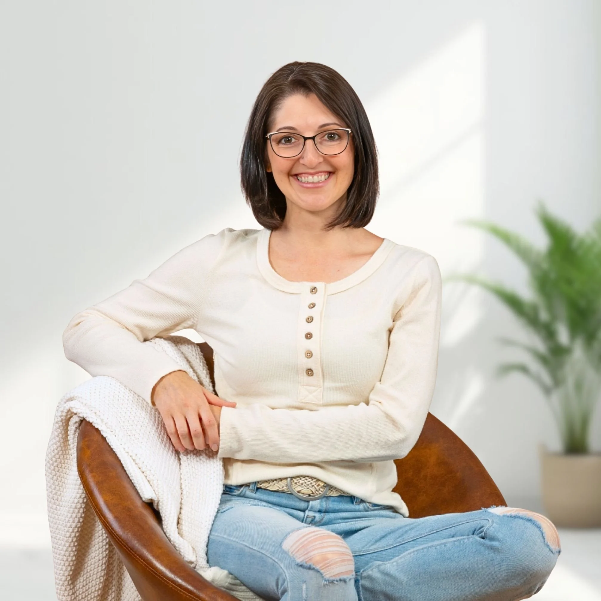 Heidi Marshall sitting in a brown leather barrel chair, smiling, wearing a cream colored shirt