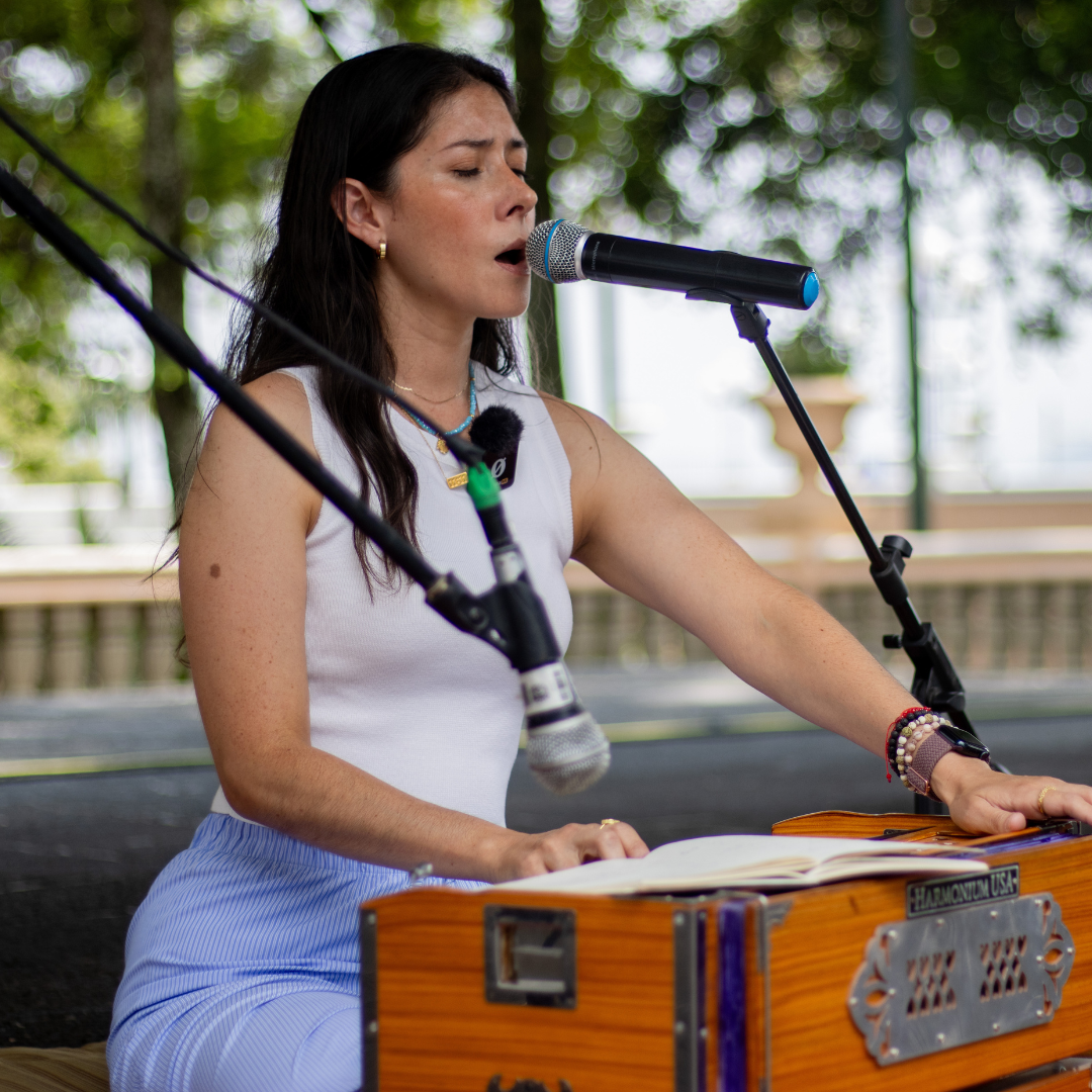 Mujer tocando el armonio y cantando con los ojos cerrados en un espacio al aire libre.