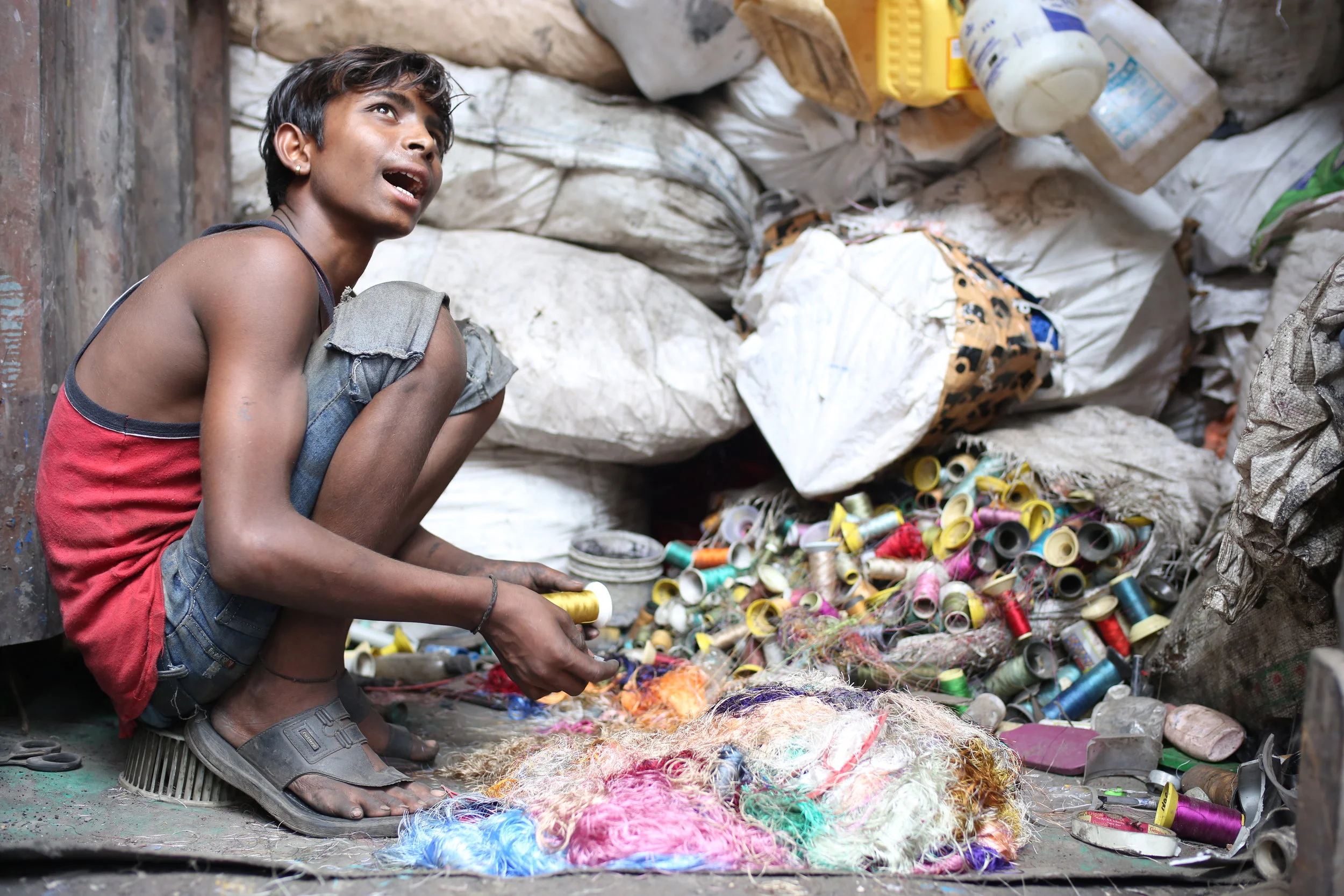  This boy works in tandem with another, slicing unwanted thread off spools so that they can sell the plastic for recycling. 
