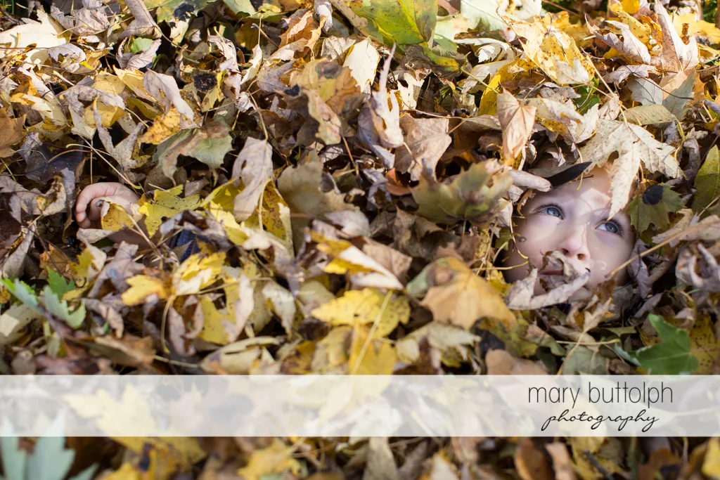 Girl covered with leaves except for her face at Skaneateles