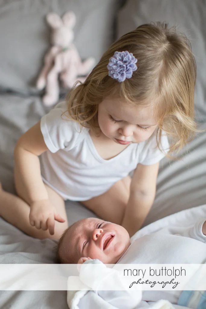 Girl can't stop her baby brother from crying in bed at Skaneateles Newborn Photography