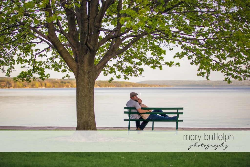 Couple relax on a bench in front of the lake at Skaneateles Engagement