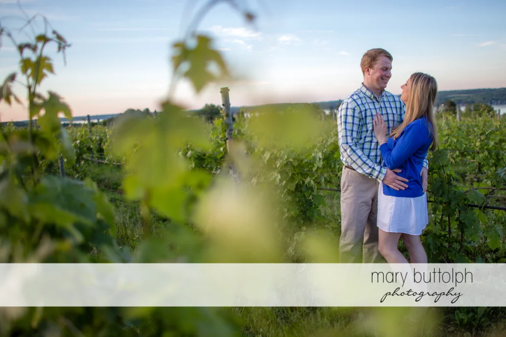 Couple pose near a fence in the field at Skaneateles Engagement
