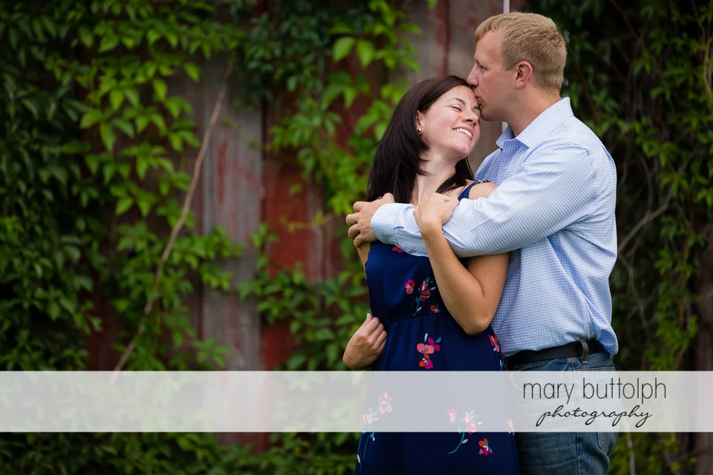 Couple pose near a wooden structure at Skaneateles Farm Engagement