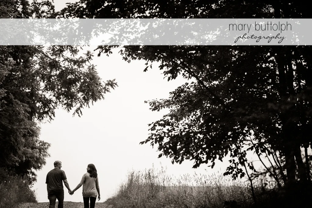 Couple walk hand in hand near the trees at Skaneateles Farm Engagement