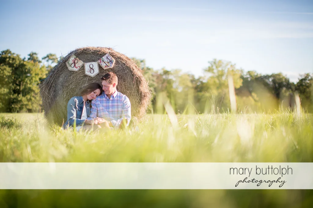 Couple sit near a haystack showing their wedding day at Aurora Engagement