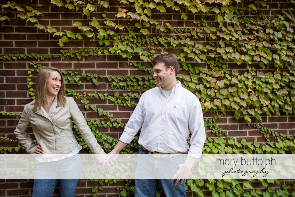 Couple hold hands in front of a brick wall at Skaneateles Engagement