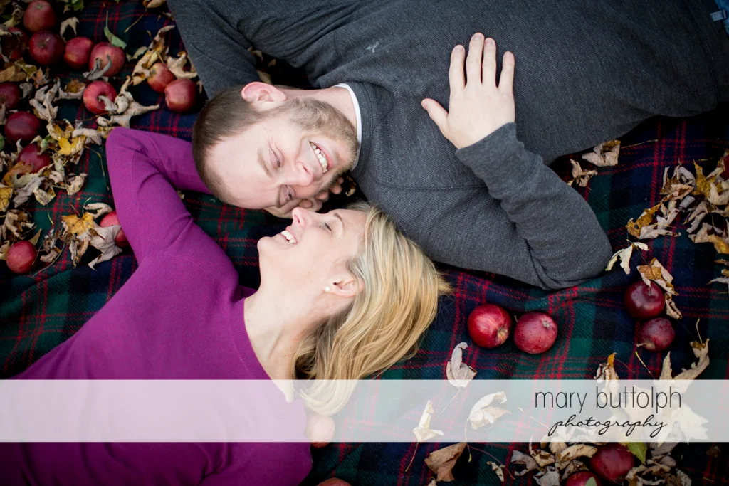 Couple lie on a blanket with apples at Beak & Skiff Apple Orchards Engagement