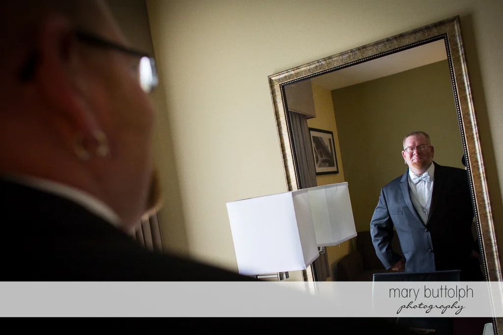 Groom looks in the mirror at Arrowhead Lodge Wedding