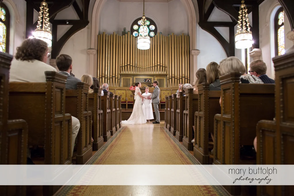 Long shot of the couple in front of the priest as guests look on at the Inns of Aurora Wedding