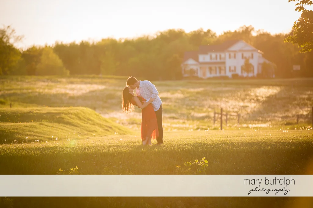 Couple kiss in the meadow in front of the hotel at Skaneateles Engagement