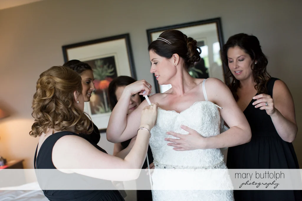Bride slips into her wedding dress with the help of friends at the Inns of Aurora Wedding