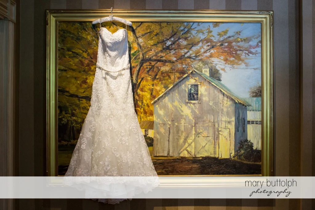 Bride's wedding dress hangs from a painting of an old barn at the Inns of Aurora Wedding
