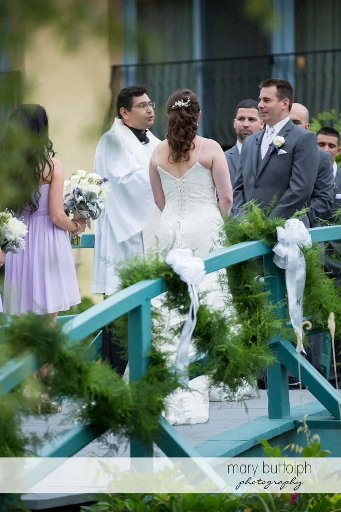 The priest talks to the couple on the bridge at the Mirbeau Inn & Spa Wedding