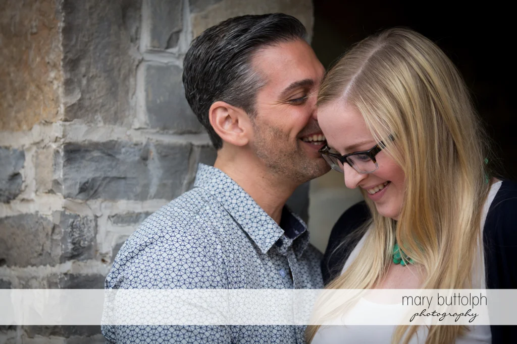 Couple can't hide their joy as they pose in front of a brick wall at Skaneateles Engagement