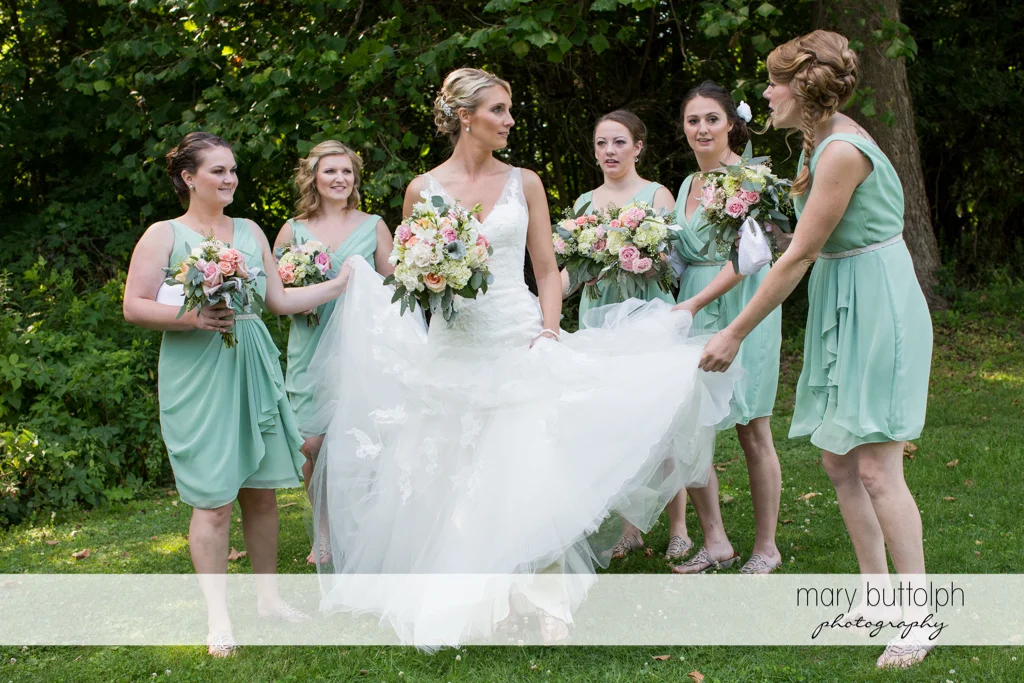 Bridesmaids hold the bride's wedding dress in the garden at Arrowhead Lodge Wedding