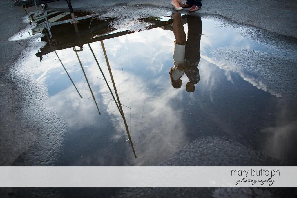 Couple's reflection is seen in a puddle of water near the lake at Skaneateles Country Club Engagement