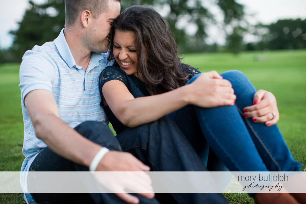 Couple sit on the grass in the park at Skaneateles Country Club Engagement
