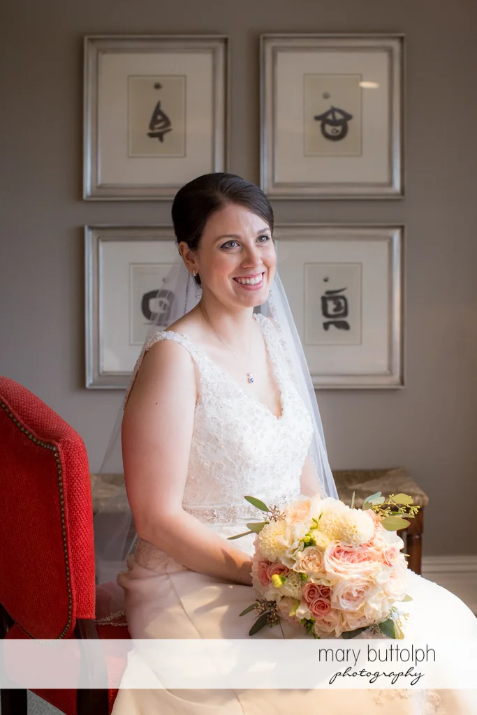 Bride with bouquet sits on a red chair at the Inns of Aurora Wedding