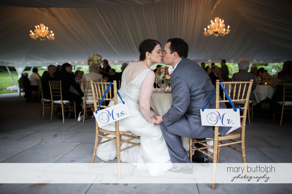 Couple kiss as they sit on designated chairs at the Inns of Aurora Wedding