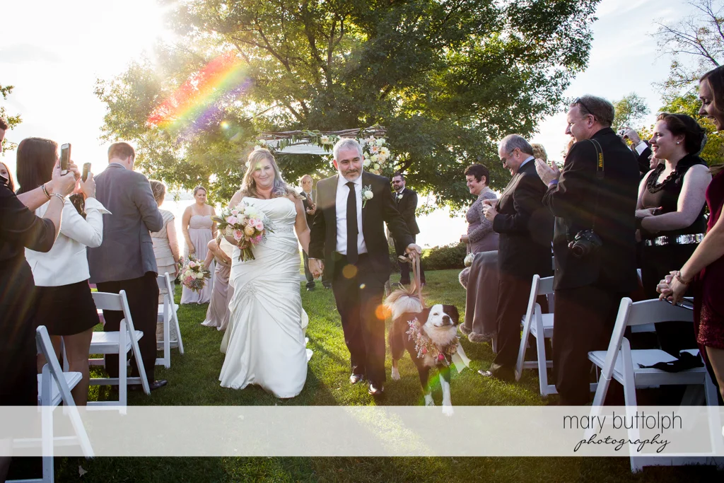 Couple with their pet dog are applauded by guests after the garden wedding at the Inns of Aurora Wedding