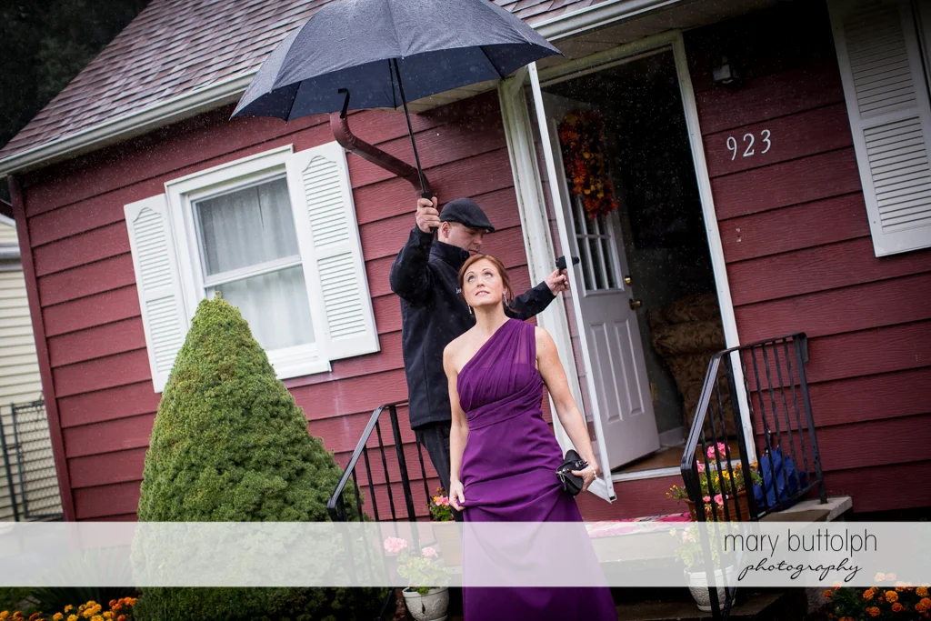 A man holds an umbrella over a bridesmaid as she steps out in the rain at the Sherwood Inn Wedding