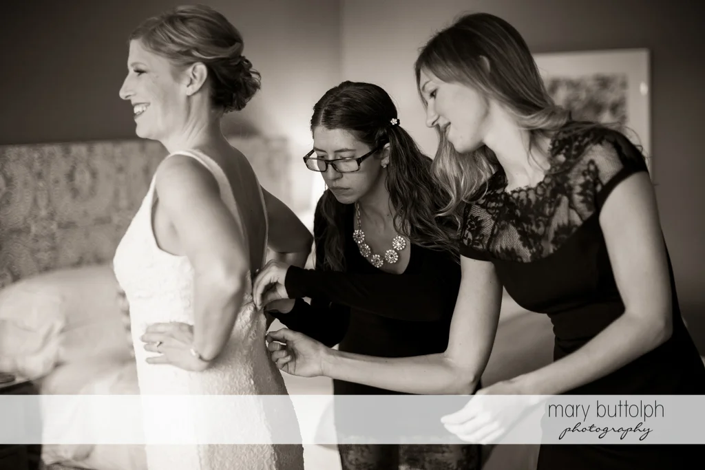 Bride slips on her wedding dress with a little from her friends at Rowland House Wedding