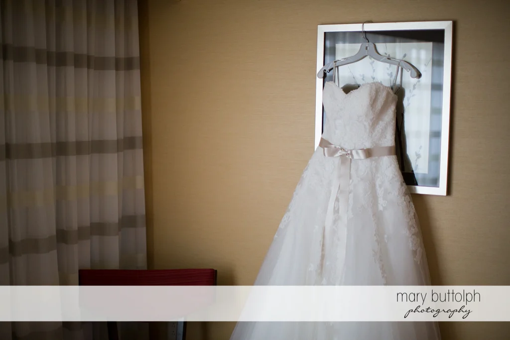 Bride's wedding gown hangs on the wall at the Lodge at Welch Allyn Wedding